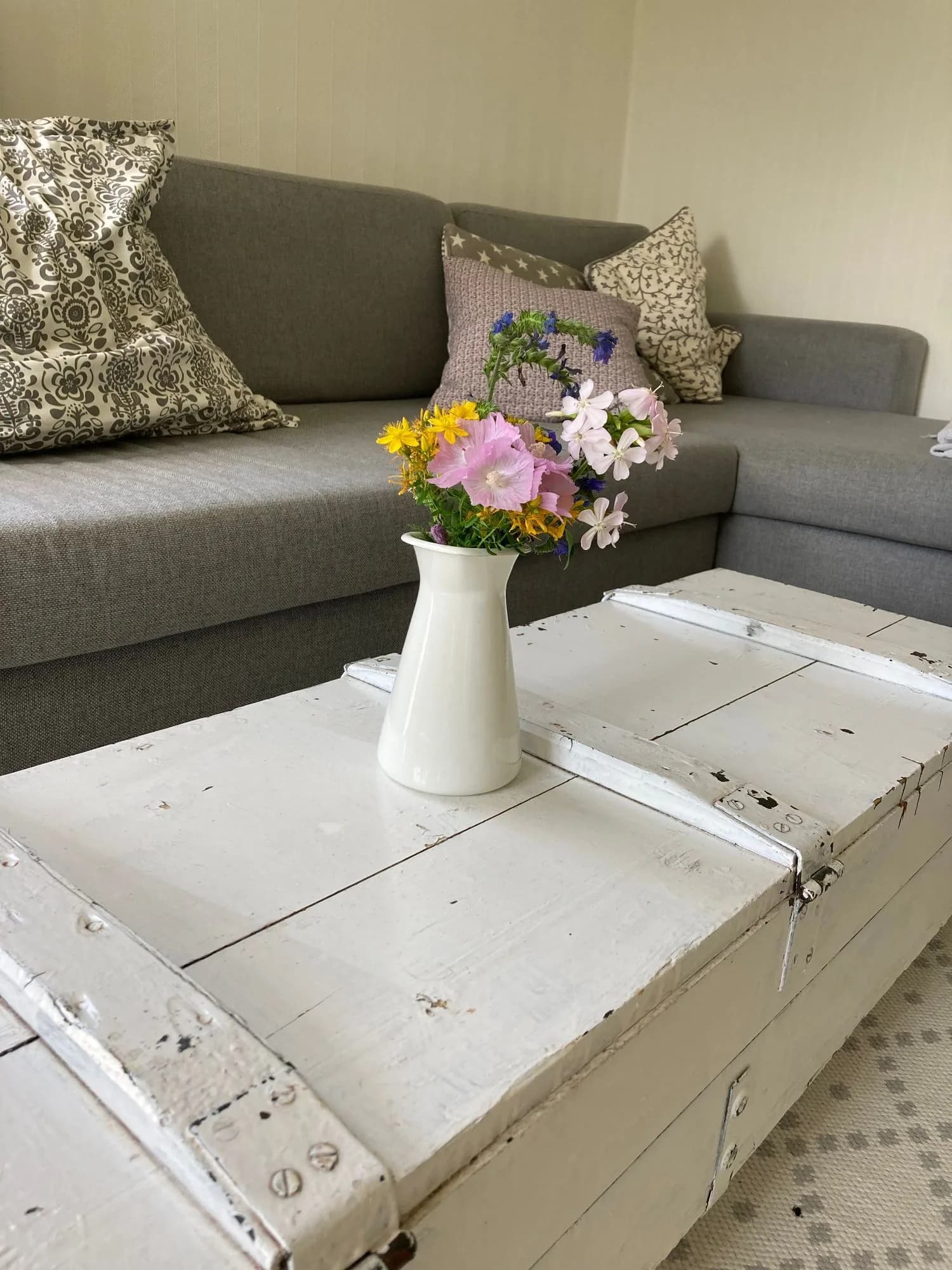 Vit träkista med vilda blommor framför en grå soffa