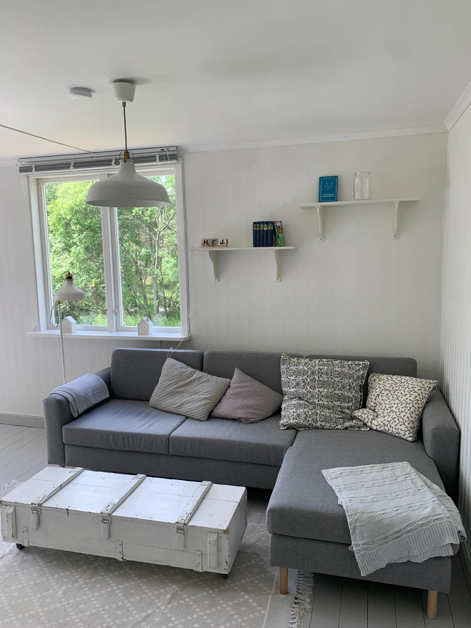 Wohnbereich mit grauem Ecksofa, weißer Holztruhe und Fenster