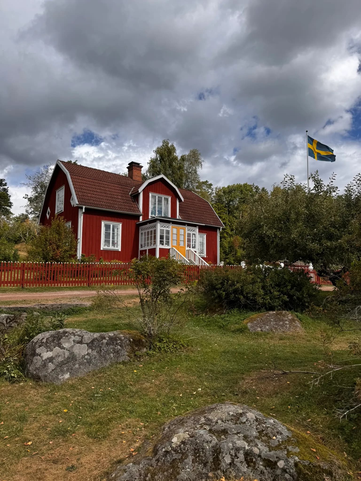 Röd träbyggnad med gul dörr och svensk flagga i Katthult